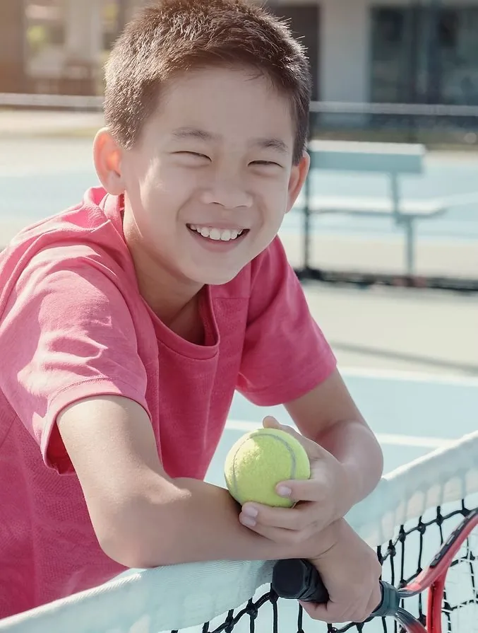 A smiling young tennis player holding a ball at the net